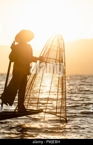 Die burmesische Fischer auf Bambus Boot, Fische zu fangen, die in traditioneller Weise mit handgefertigten net. bei Sonnenuntergang. Inle See, Myanmar (Birma) Reiseziel Stockfoto