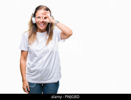 Mittleres Alter Hispanic Frau Musikhören mit Kopfhörern über isolierte Hintergrund tun ok Geste mit der Hand lächelnd, Auge durch finge Stockfoto