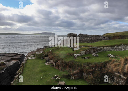 Midhowe Broch auf einer Landzunge auf Rousay Insel, mit Blick auf die raue Gewässer in Eynhallow Sound und Orkney Mainland, in Schottland; eine tiefe Geo ist auf der linken Seite Stockfoto