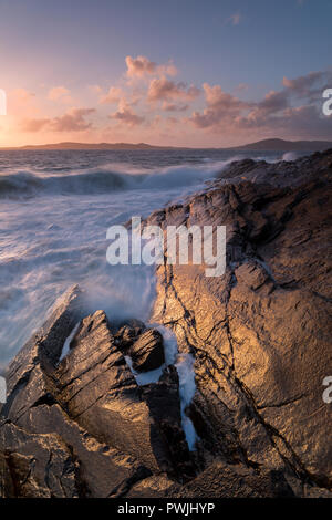 Wellen über die nassen Felsen auf Harris bei Sonnenuntergang zu brechen. Goldenes Licht auf den Felsen Stockfoto