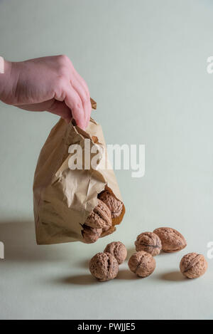 Beschädigte shopping Papiertüte in der Hand einer Frau. Die Walnüsse aus Papier Beutel fallen auf dem grünen Tisch Stockfoto