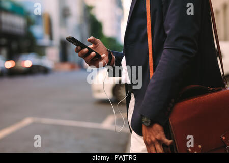 7/8 Schuß von Geschäftsmann Walking im Freien mit Handy. Mann in Anzug mit Handtasche Wandern auf Stadt Straße mit Handy in der Hand.