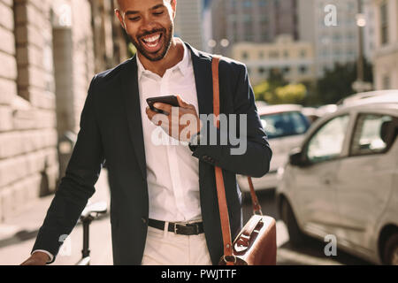 Hübscher junger Mann mit Anzug zu Fuß mit seinem Fahrrad im Freien und Gespräch am Handy. Afrikanischen Geschäftsmann, Büro und Telefon. Stockfoto