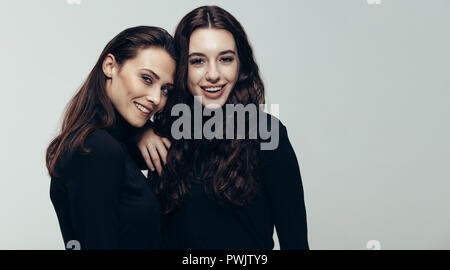 Porträt von zwei junge Frau im schwarzen Outfit an der Kamera zu lächeln. Zwei weibliche Freunde gemeinsam gegen grauer Hintergrund Stockfoto