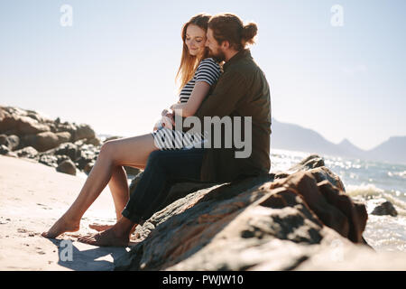 Junger Mann und Frau sitzen zusammen auf den Felsen entlang der Küste. Romantisches junges Paar am Strand zu entspannen. Stockfoto