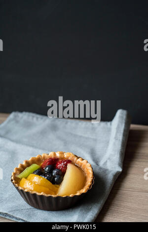 Weite Einstellung auf ein mini Obstkuchen auf einem blauen Tuch Serviette vor einem dunklen Hintergrund Stockfoto