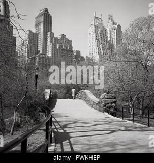 1950, historische, Dame, die kleine Brücke im Central Park, New York, USA, zu Fuß in Richtung der Wolkenkratzer von Manhattan, New York City in der Ferne. Stockfoto