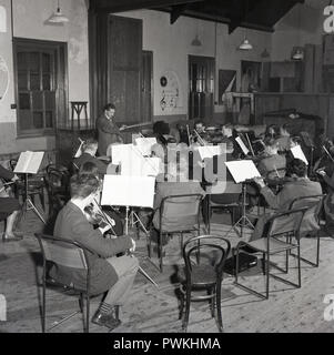 1950, historische, Mitglieder oder Spieler von einem Amateur Dorf Orchester unter der Leitung von Dirigent, zusammen zu praktizieren in einer Pfarrei oder Gemeinschaft Hall, England, UK. Amateur Musik war, zusammen mit laienhaften Dramatik, einem beliebten Freizeitaktivitäten und soziale Tätigkeit für viele Erwachsene in einer trostlosen post-ww2 Großbritannien. Stockfoto