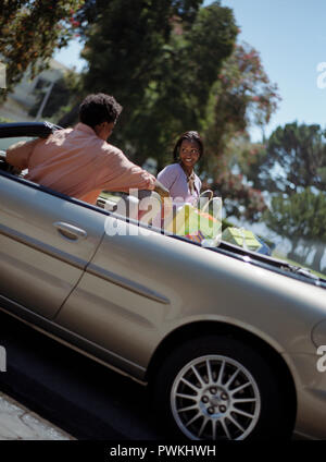 Glückliche junge Frau an ihrem Freund, der in einem Auto voller Einkaufstaschen sitzt lächelnd. Stockfoto