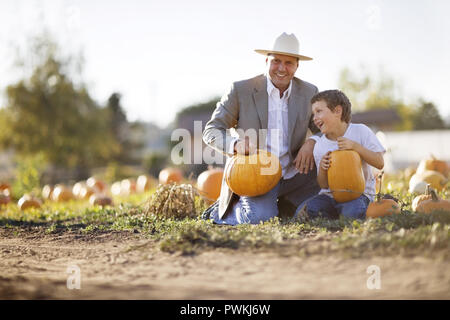 Porträt eines lächelnden Mitte erwachsenen Mann hält einen Kürbis sitzend, mit seinem Sohn ein kürbisfeld, Stockfoto