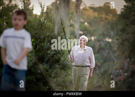 Ältere erwachsene Mann zu Fuß durch Buschland eine Angelrute mit seiner jungen Enkel. Stockfoto