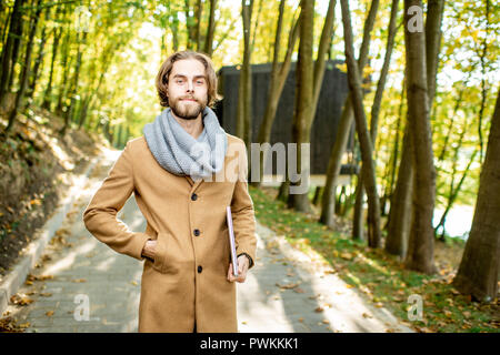 Porträt einer stilvollen Mann im Mantel und Schal stand draußen im Wald im Herbst Zeit Stockfoto