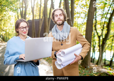 Kreative Paar der Architekten oder Designer arbeiten mit Laptop und Zeichnungen draußen im Wald Stockfoto