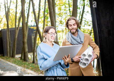 Kreative Paar der Architekten oder Designer arbeiten mit Laptop und Zeichnungen draußen im Wald Stockfoto