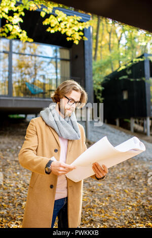 Porträt eines gutaussehenden Mann Architekt stehend mit Zeichnungen vor der moderne Häuser im Wald Stockfoto