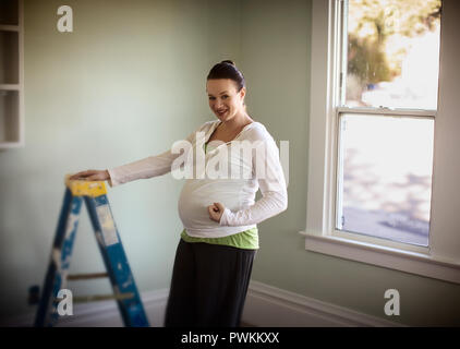 Seitenansicht einer schwangeren Frau stand neben einem Fenster. Stockfoto