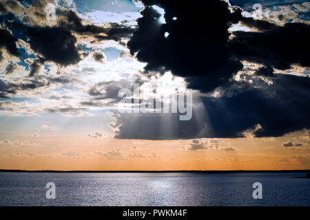 Große schwarze Schwarm und eine Menge Wolken die Sonne, Sonnenstrahlen, die sich über den Himmel, die schwarzen Horizont trennt den Himmel und das Wasser Stockfoto