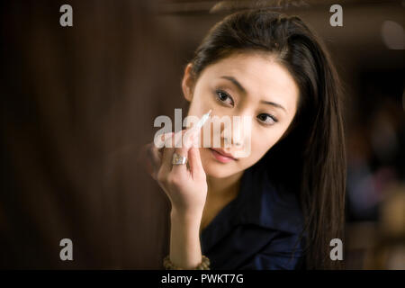 Junge erwachsene Frau Anwendung Make-up Während in einem Spiegel zu betrachten. Stockfoto
