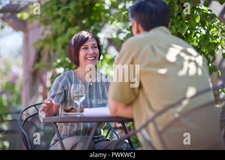 Lächelnd Mitte der erwachsenen Frau über einen Tisch in einem Mann auf der Suche beim Sitzen im Freien in einem Restaurant. Stockfoto