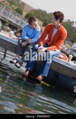 Gerne Mitte der erwachsenen Frau und ihr Sohn sitzt auf der Kante einer Anlegestelle. Stockfoto
