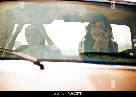 Zwei weibliche Freunde sitzen in einem Pick-up-Truck, Anwendung von Make-up im Rückspiegel. Stockfoto