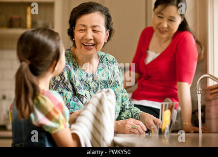 Lächelnde ältere Frau von ihrer enkelin in der Küche geholfen wird. Stockfoto