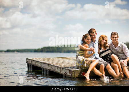 Gruppe von Freunden sitzen auf einem Steg, Planschen im See mit ihren Beinen. Stockfoto