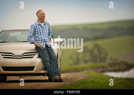 Lächelnd im mittleren Alter Mann lehnte sich auf der Motorhaube seines Autos. Stockfoto