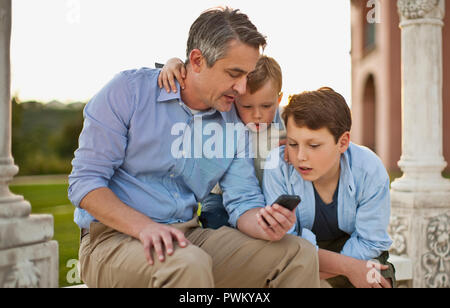 Reifer Mann sein Handy zu zeigen seine neugierigen Kinder. Stockfoto