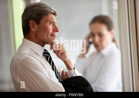 Reifen Geschäftsmann mit verschränkten Armen und Ruhen, sein Kinn auf seine Hand wartet nachdenklich als Kollegin einen Anruf auf ein Mobiltelefon. Stockfoto