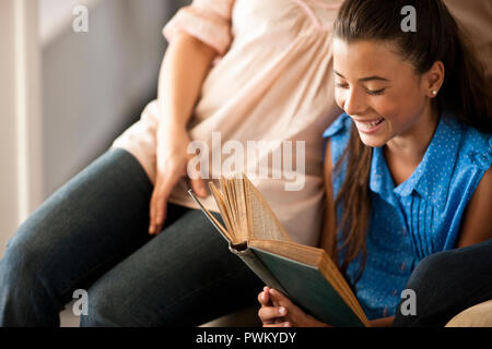 Junge Mädchen Lesen auf einem Sessel mit ihrer Mutter neben ihr sitzt. Stockfoto