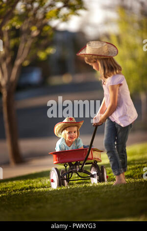 Mädchen ziehen ihre jüngere Schwester in einem roten Wagen. Stockfoto