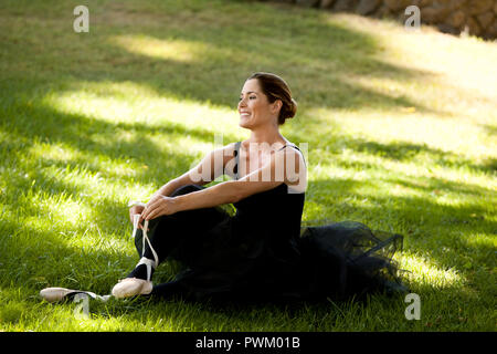 Mitte der erwachsenen Frau sitzen und Lächeln in einem Park beim Tragen eines Ballett Kostüm. Stockfoto