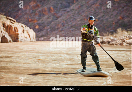 Lächelnd Mann unten paddleboarding ein Fluss. Stockfoto