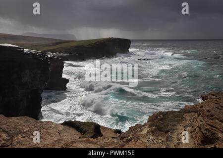 Dramatische Wellen entlang der Klippen am Festland Yesnaby, Orkney, Schottland, UK, als ein Sturm weht aus dem Nordatlantik, Regen und Hoy in der Ferne. Stockfoto