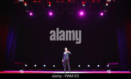 Showman. Junger männlicher Entertainer, Moderator und Schauspieler auf der Bühne. Rücken, Arme an den Seiten, Rauch auf dem Hintergrund von Spotlight. Rückansicht eines männlichen öffentliche Redner am Mikrofon, zeigen, in der. Stockfoto