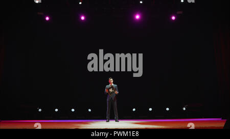 Showman. Junger männlicher Entertainer, Moderator und Schauspieler auf der Bühne. Rücken, Arme an den Seiten, Rauch auf dem Hintergrund von Spotlight. Rückansicht eines männlichen öffentliche Redner am Mikrofon, zeigen, in der. Stockfoto