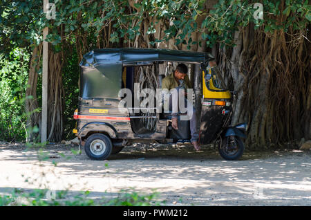 Eine Auto-rikscha Fahrer warten für Kunden unter dem Schatten der Banyan Tree in Hampi, Karnataka, Indien. Stockfoto