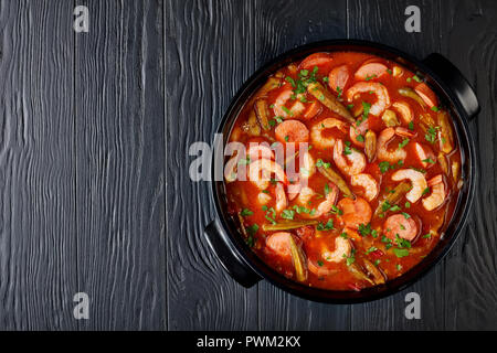 Ansicht von oben der Köstlichen Gumbo mit Garnelen, Würstchen in einem holländischen Ofen auf einem Schwarzen Tisch, horizontale Ansicht von oben, flach Stockfoto