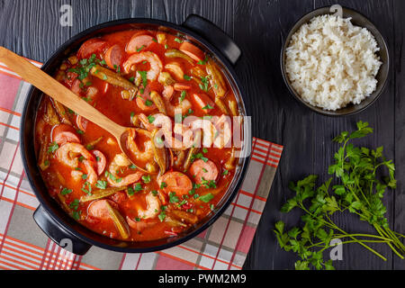 Ansicht von oben der köstlichen Gumbo mit Garnelen, Okra, Wurst in einem holländischen Ofen auf einem Schwarzen Tisch mit Schale, weißer Reis, horizontale Ansicht von oben, Clos Stockfoto