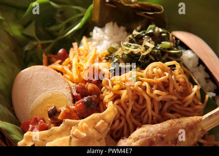 Nasi Jinggo, die Balinesische kleine Mahlzeit aus Reis mit gebratenen Nudeln, Gemüse und Ei umhüllt mit Banana Leaf; mit zusätzlichen optionalen Beilagen serviert. Stockfoto