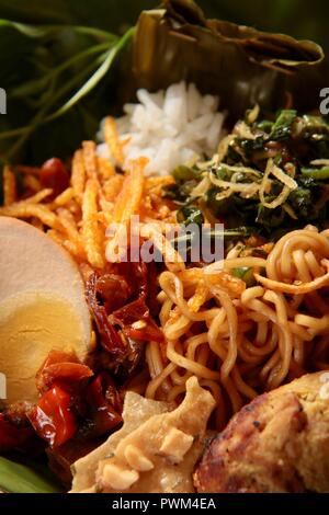 Nasi Jinggo, die Balinesische kleine Mahlzeit aus Reis mit gebratenen Nudeln, Gemüse und Ei umhüllt mit Banana Leaf; mit zusätzlichen optionalen Beilagen serviert. Stockfoto