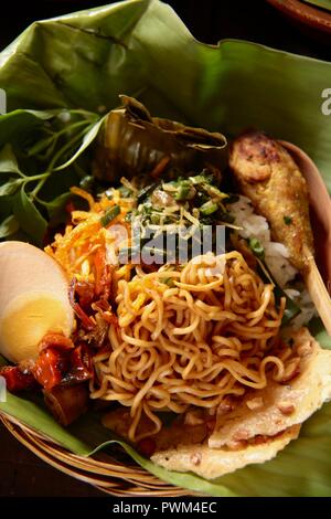 Nasi Jinggo, die Balinesische kleine Mahlzeit aus Reis mit gebratenen Nudeln, Gemüse und Ei umhüllt mit Banana Leaf; mit zusätzlichen optionalen Beilagen serviert. Stockfoto