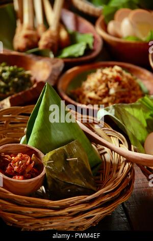 Nasi Jinggo, die Balinesische kleine Mahlzeit aus Reis mit gebratenen Nudeln, Gemüse und Ei umhüllt mit Banana Leaf; mit zusätzlichen optionalen Beilagen serviert. Stockfoto