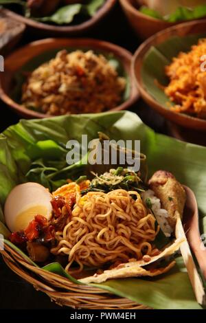 Nasi Jinggo, die Balinesische kleine Mahlzeit aus Reis mit gebratenen Nudeln, Gemüse und Ei umhüllt mit Banana Leaf; mit zusätzlichen optionalen Beilagen serviert. Stockfoto