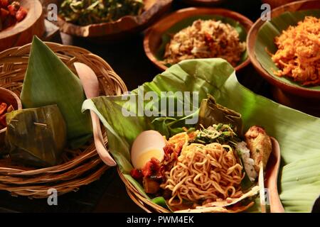 Nasi Jinggo, die Balinesische kleine Mahlzeit aus Reis mit gebratenen Nudeln, Gemüse und Ei umhüllt mit Banana Leaf; mit zusätzlichen optionalen Beilagen serviert. Stockfoto