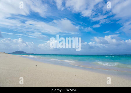 Low Angle Shot eines ruhigen Strandes in Hawaii mit sanften Wellen auf das türkisfarbene Meer und blauer Himmel mit weißen Wolken über verstreut auf einem sonnigen breezy Tag Stockfoto