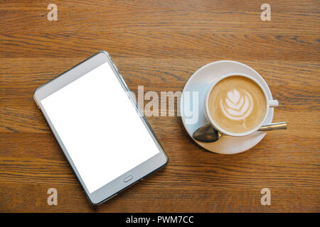 Cappuccino in einem Becher auf den Tisch neben einem Tablet mit einem leeren weißen Bildschirm. Stockfoto