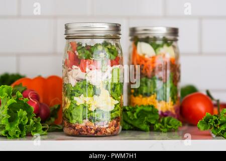 Zwei 2-in-1-Salate, die in Gläsern mit Spinat, Bohnen, Käse und Eier Stockfoto