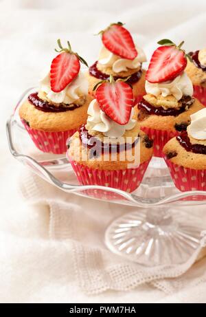 Mehrere frische Erdbeeren mit Sahne Cupcakes auf einem Glas Kuchen stehen mit cremefarbenen naplin und Stoff Stockfoto